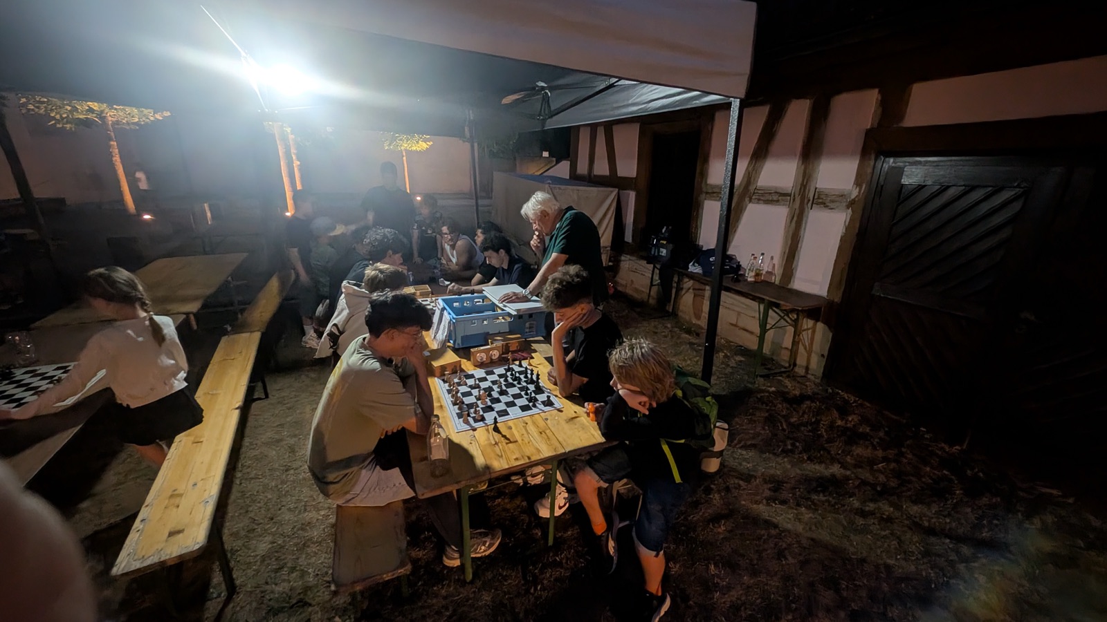 Jugendliche spielen abends unter einem Pavillon Schach, ein Vereinsmitglied schaut zu