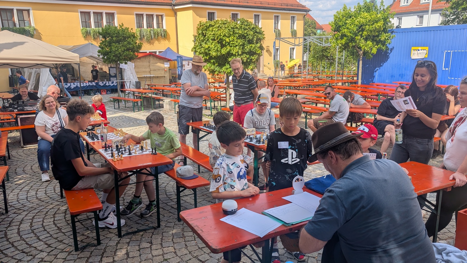 Kinder und Jugendliche spielen an Biertischgarnituren auf dem Kammereckerplatz Schach, umgeben von Zuschauern