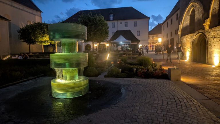 Der beleuchtete Brunnen auf dem Münsterplatz in der Abenddämmerung, im Hintergrund das Münster und Festzelte