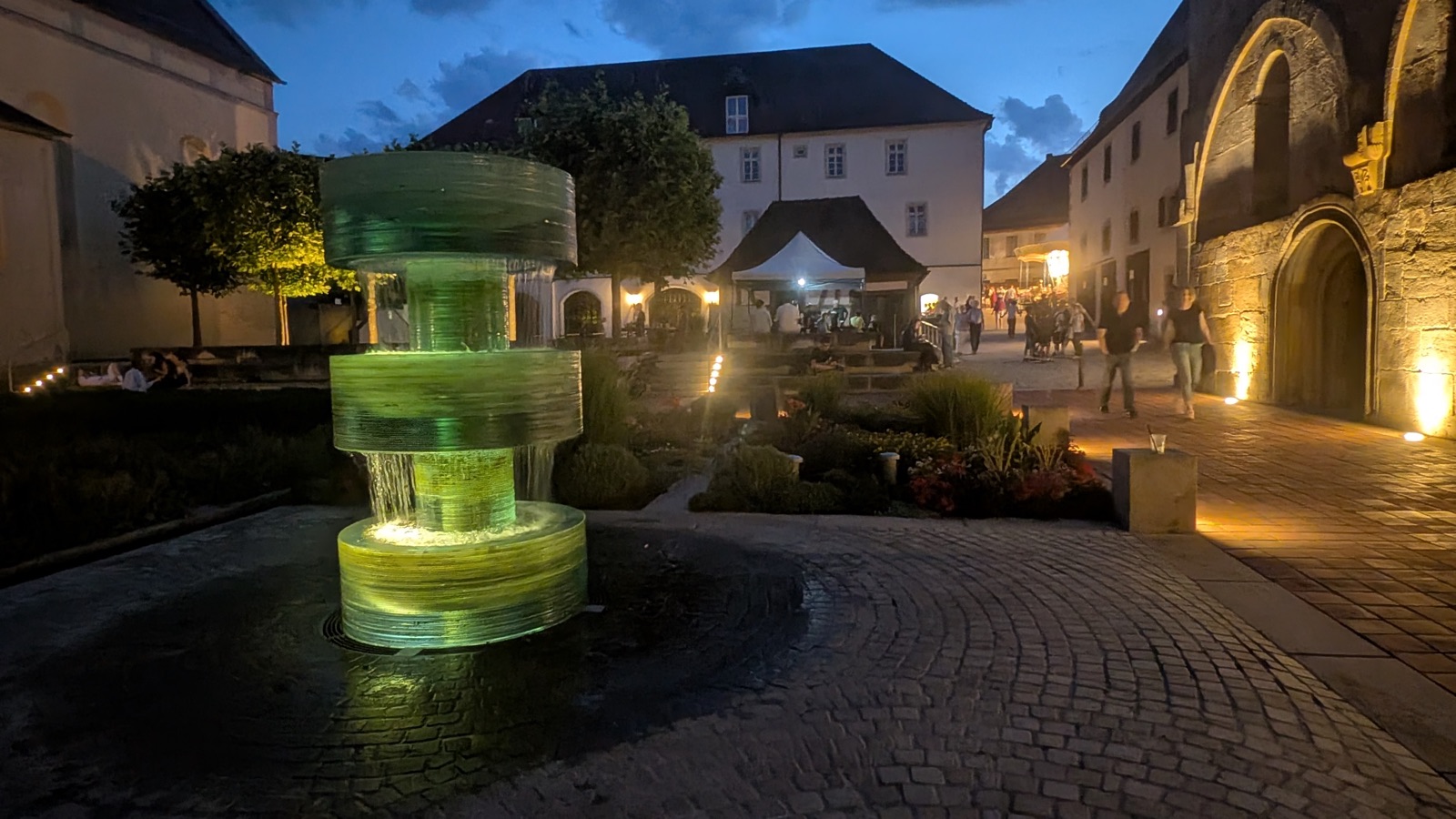 Der beleuchtete Brunnen auf dem Münsterplatz in der Abenddämmerung, im Hintergrund das Münster und Festzelte
