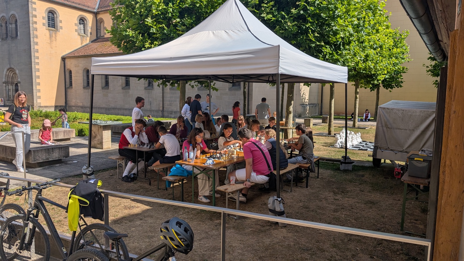 Besucher aller Altersgruppen spielen unter einem weißen Pavillon Schach, daneben ein Gartenschach